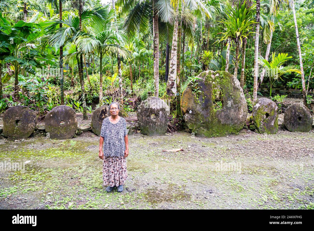 Yap island, Micronesia - Aug 04 2015: Local Micronesian older native women standing in the jungle by a bank of Yapese stone money rai. Federated State Stock Photo