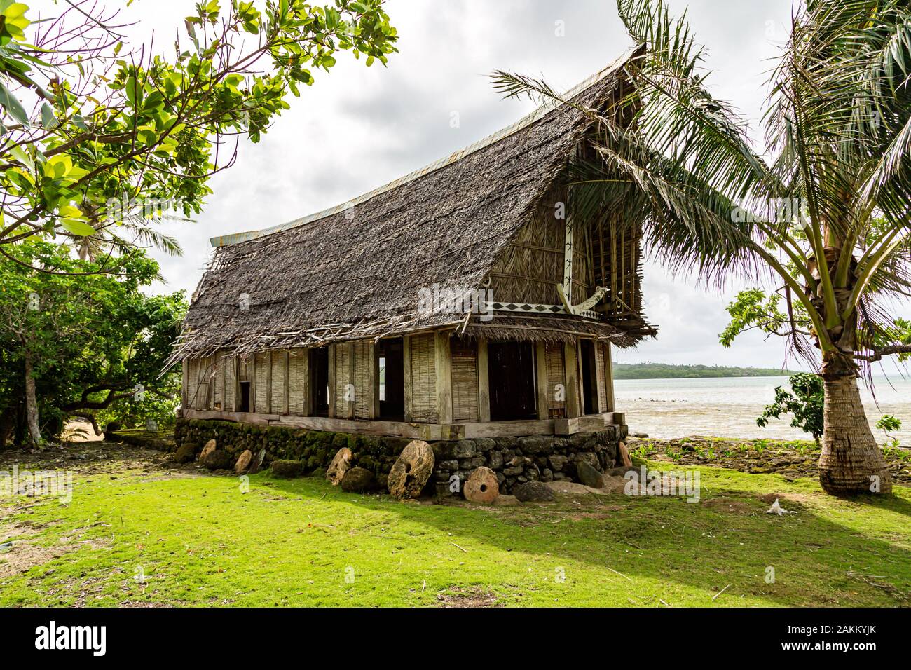 Old traditional thatched yapese men's meeting house faluw or fale, on an elevated limestone platform with bank of rai stone money. Shore of South Paci Stock Photo