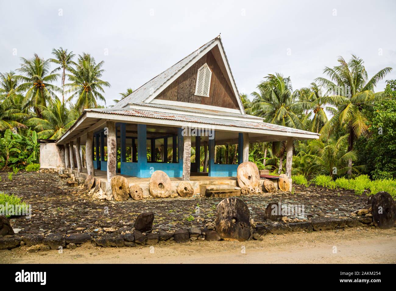 Traditional thatched yapese men's meeting house called faluw or fale and a bank of three historic megalithic stone money rai in front of it. A high co Stock Photo