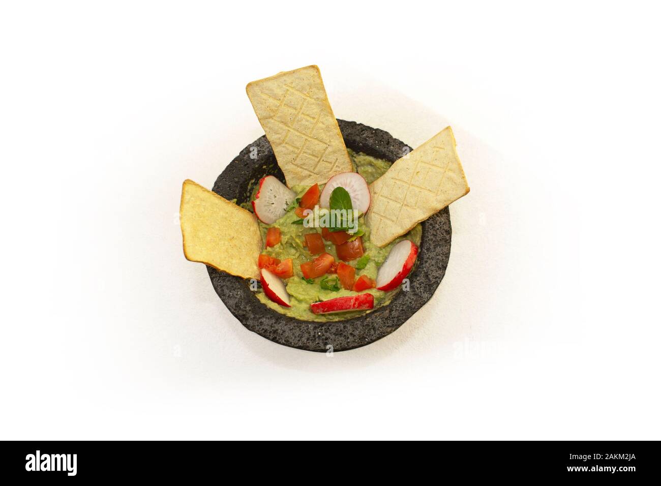 Mexican food gourmet dish Green Guacamole sauce served in stone mortar with ingredients such as tomato, onion, coriander, peppermint, avocado and cris Stock Photo