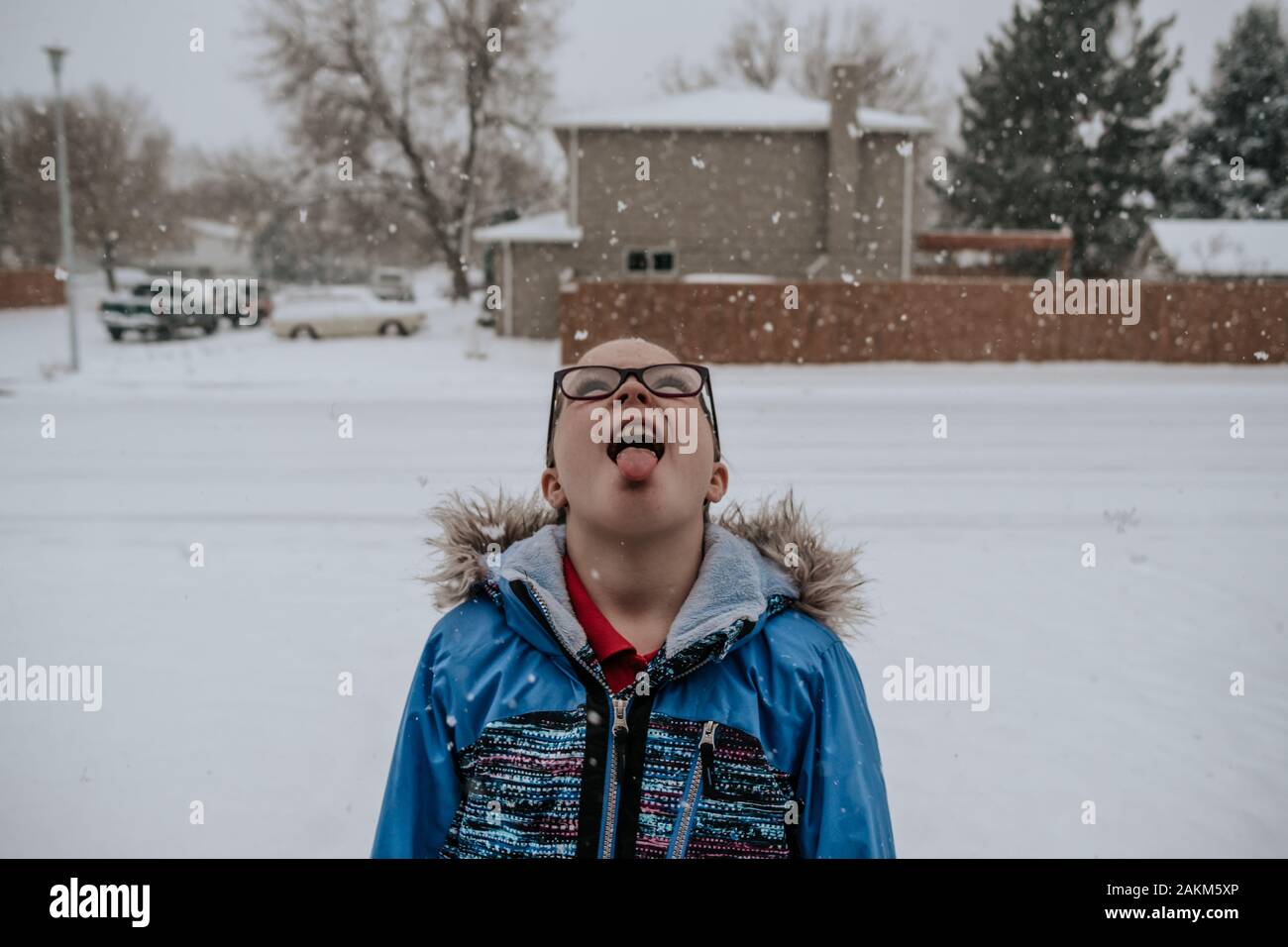 portrait of girl catching snow flakes on tongue in front yard Stock Photo