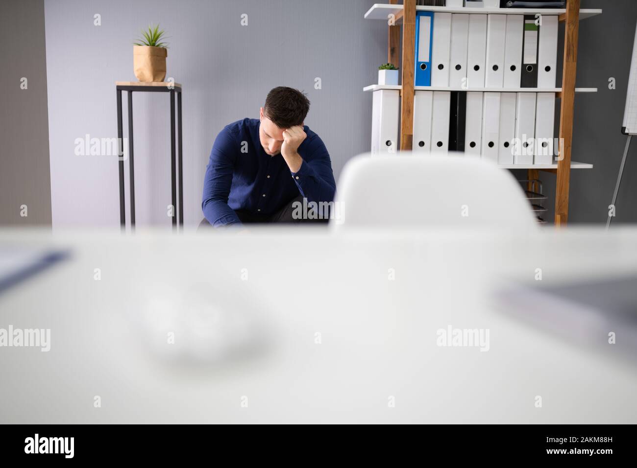 Sad Young Man Sitting At The Floor Of The Room At Office Stock Photo
