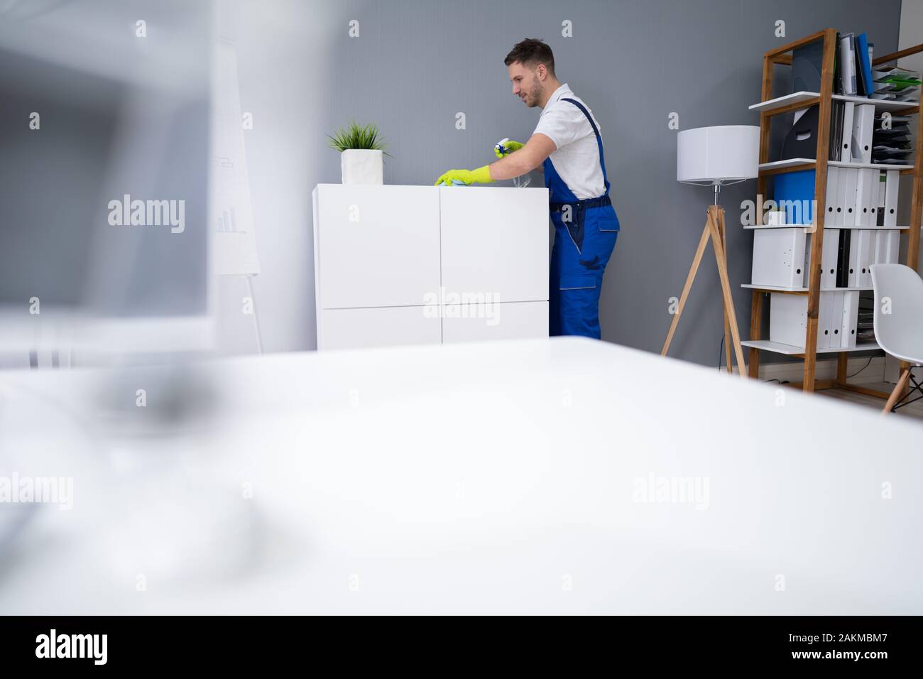 Mid Adult Male Worker Cleaning Shelf With Spray And Sponge At Office Stock Photo