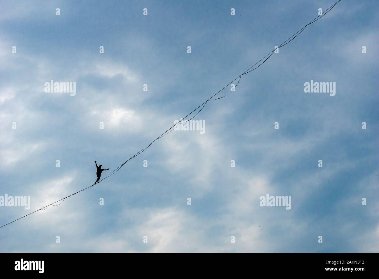 A man walking on strecthed sling - performance of a tightrope walker with background of dramatic clouds. Man balances over the abyss Stock Photo