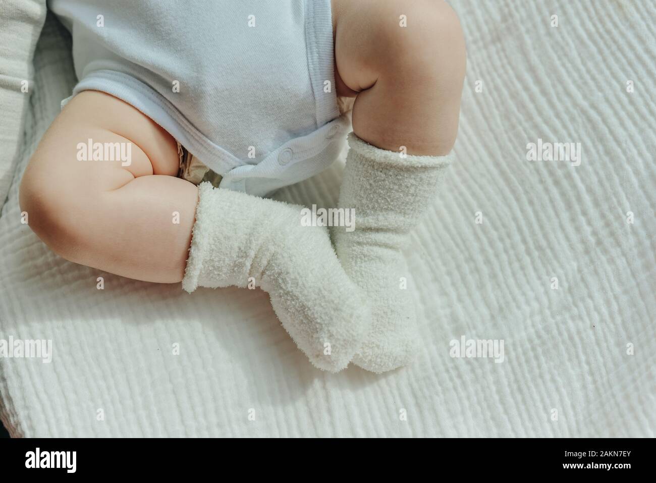 Baby legs. Crawling baby in white socks and bodysuit. View from above