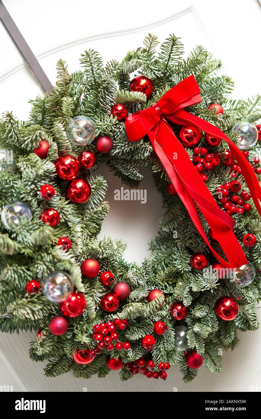 Beautiful red Christmas wreath of fresh spruce on the white door. Entrance to the house. Christmas mood. Xmas tree. Stock Photo