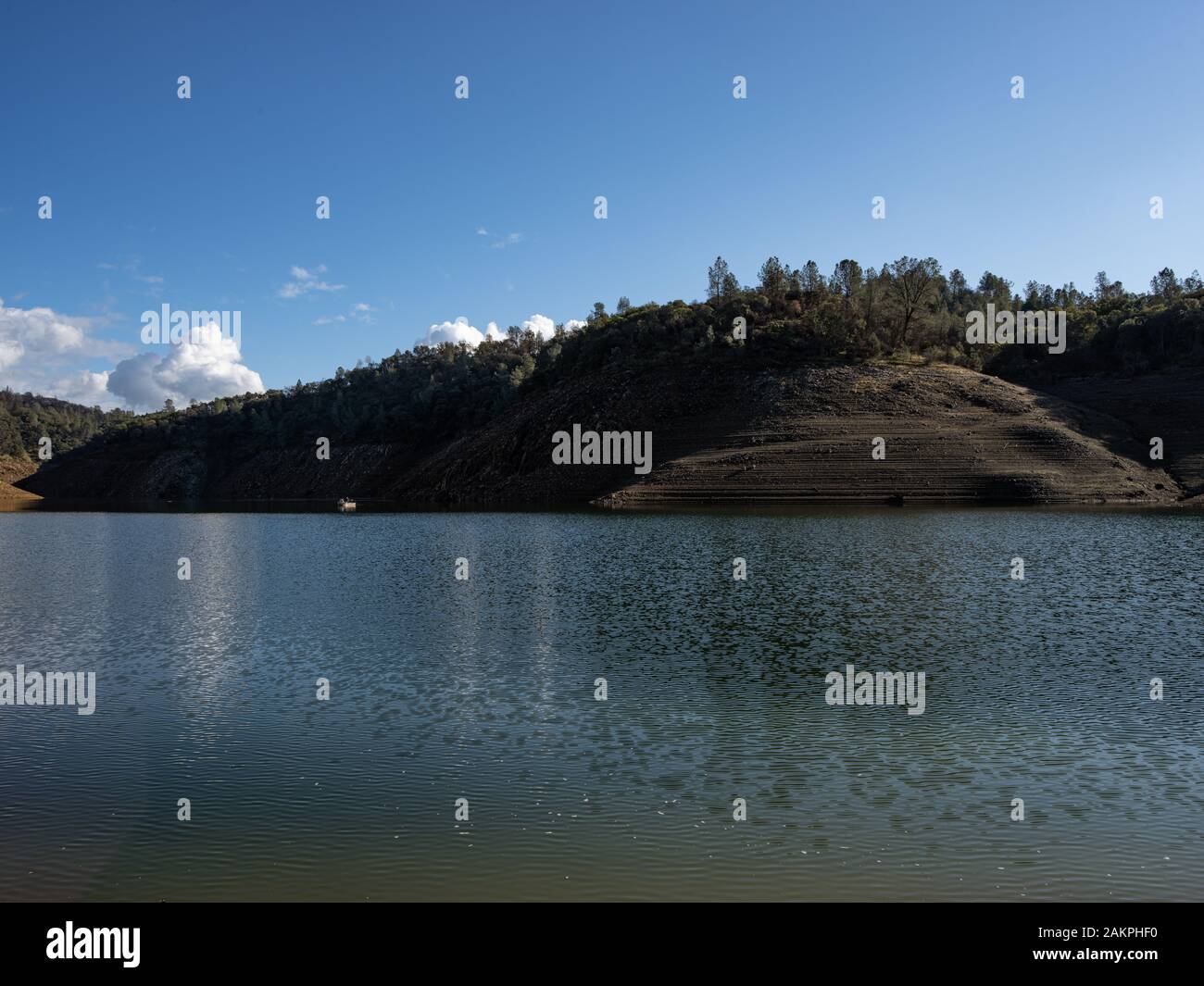 Theres a boat peaking out of the shadow of the hill on the lake. Stock Photo