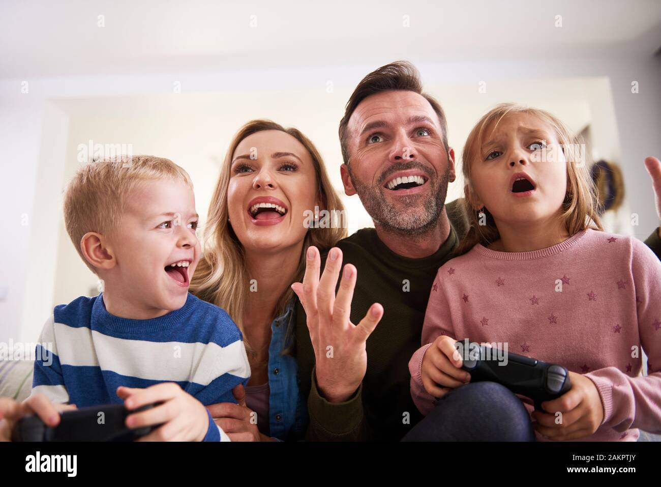 Emotional parents and children playing video game at home Stock Photo