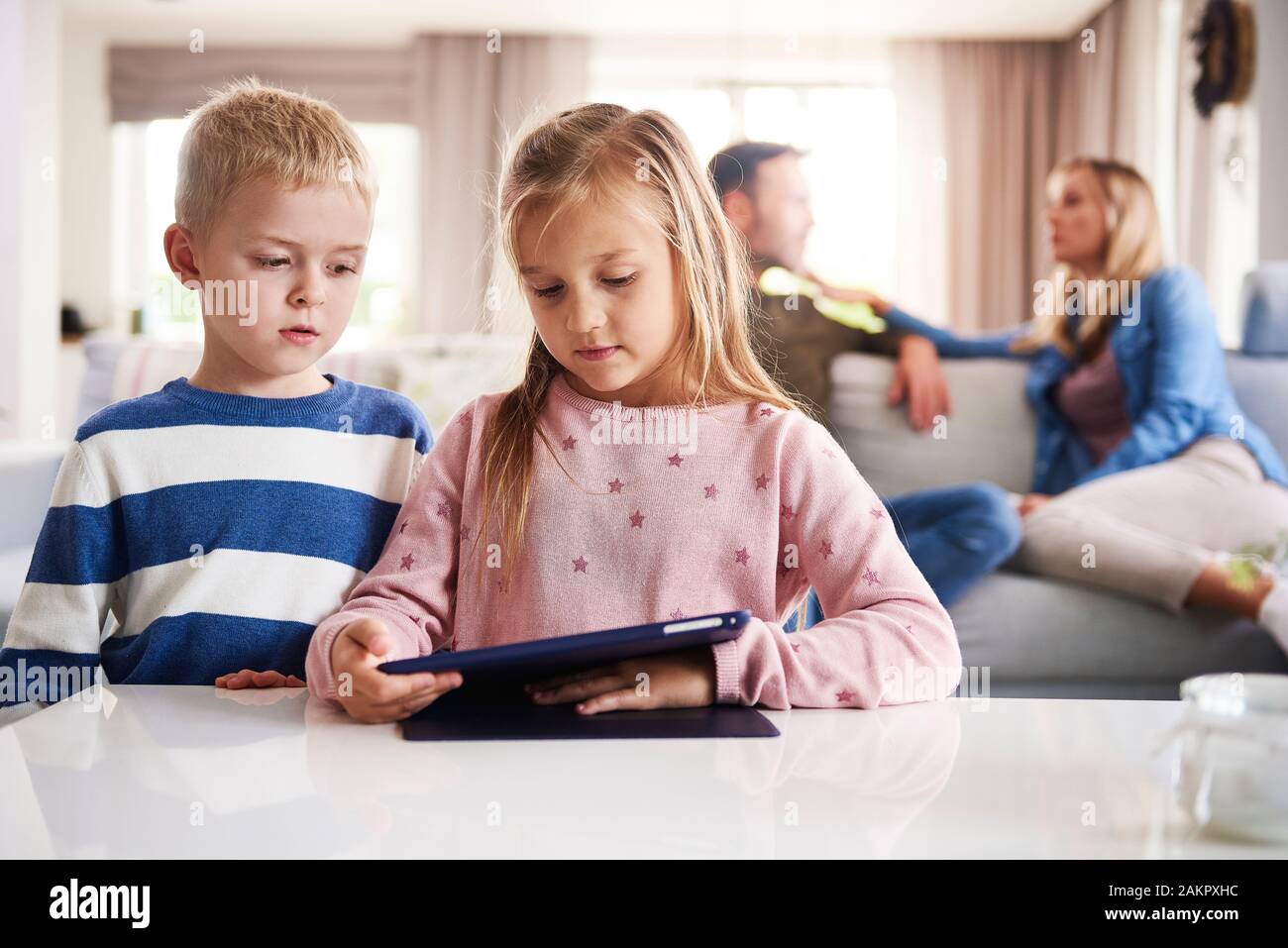 Focused children using technology and parents in the background Stock Photo