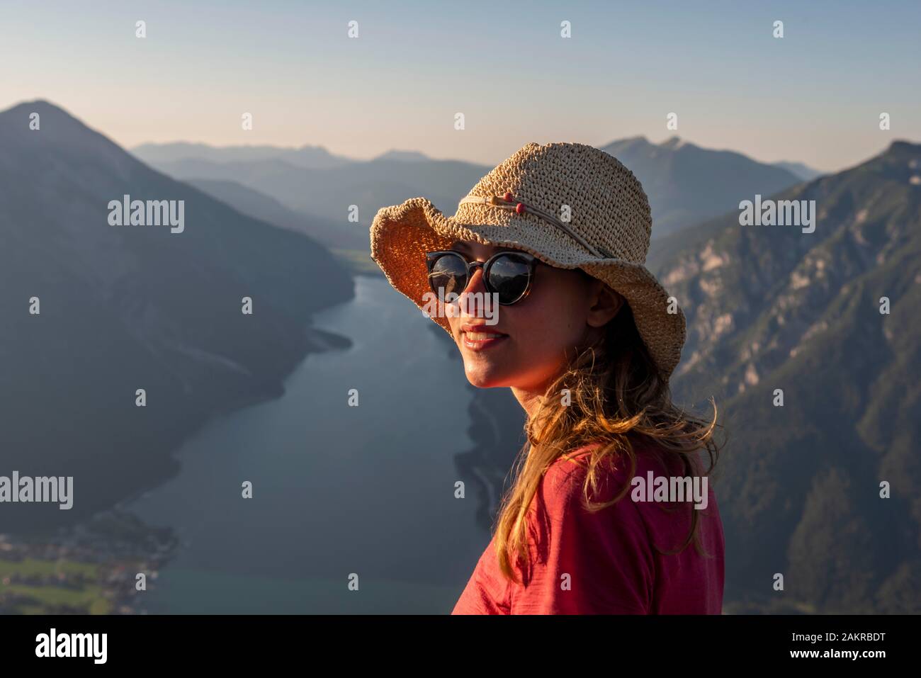 Young woman with sunglasses and sun hat, in the back mountain landscape with Lake Achensee, view from the mountain Baerenkopf, Tyrol, Austria Stock Photo