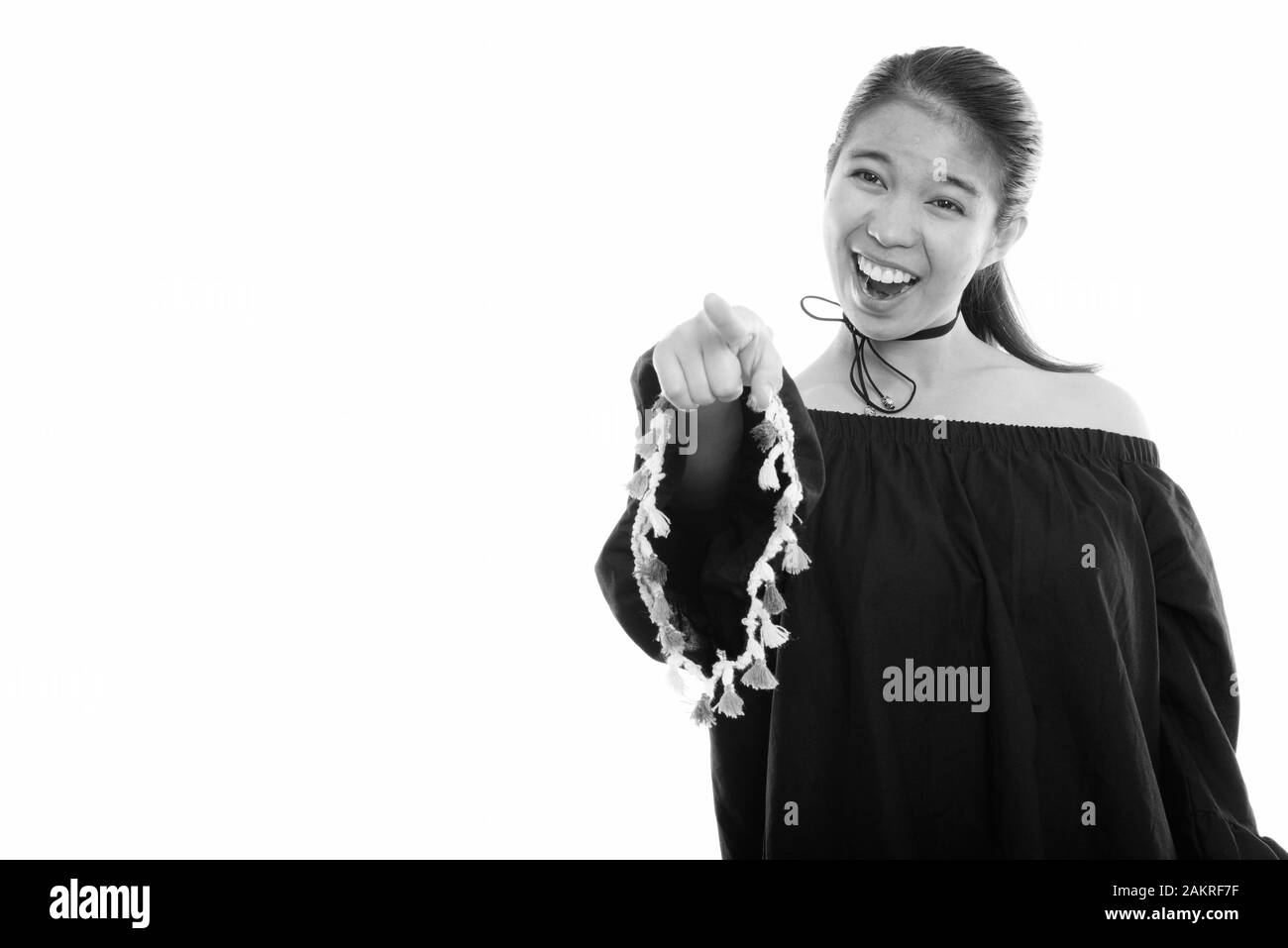 Studio shot of young happy Asian woman smiling while laughing and pointing at distance Stock Photo
