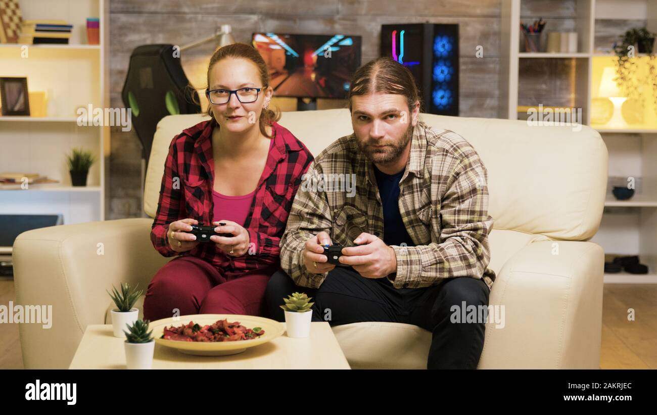 Zoom in shot of beautiful young couple playing video games sitting on couch using controllers. Stock Photo