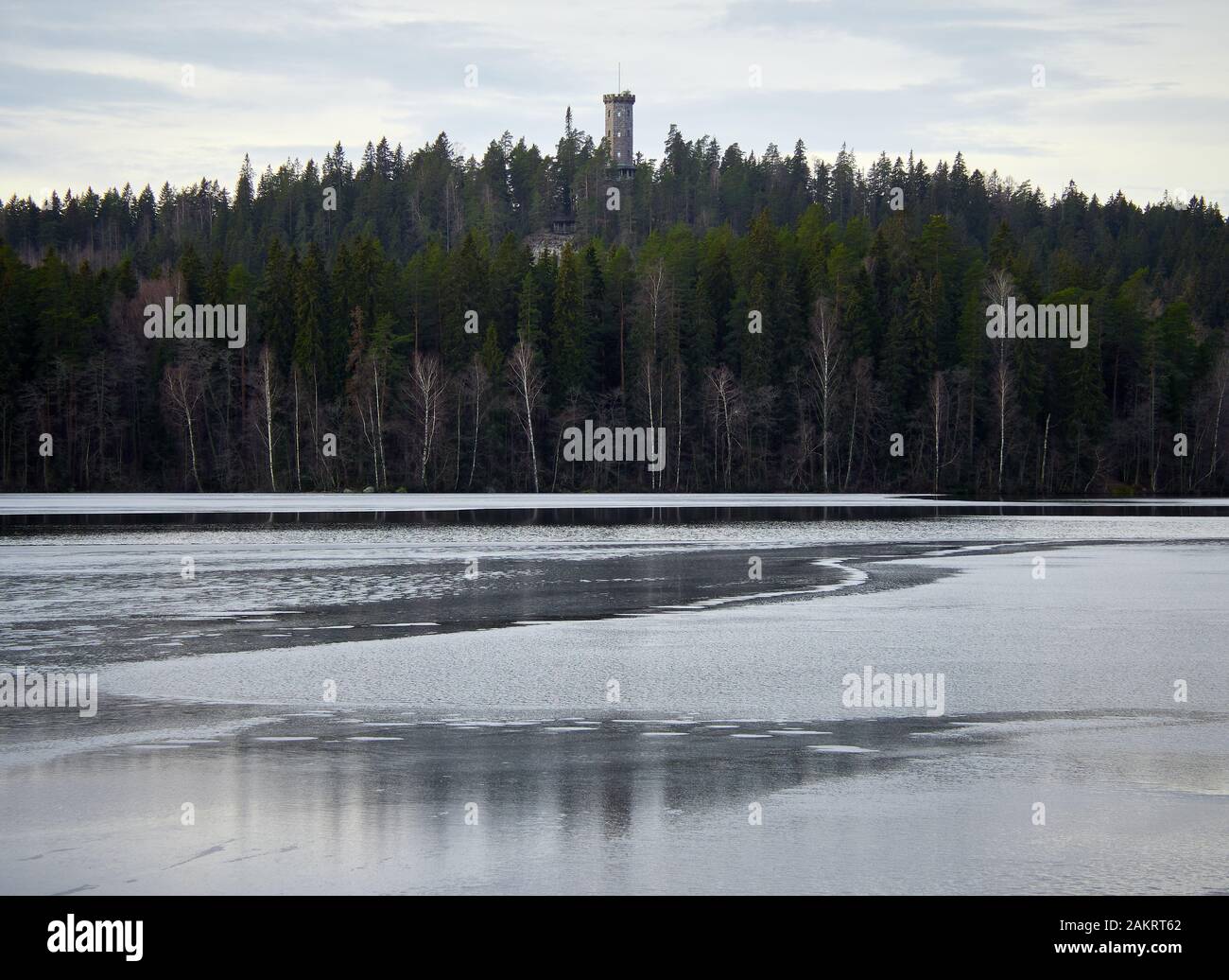 Late autumn landscape at Aulanko nature park in Finland. Reflection of the scene and the lookout tower in the still and icy water of the Aulangonjarvi Stock Photo