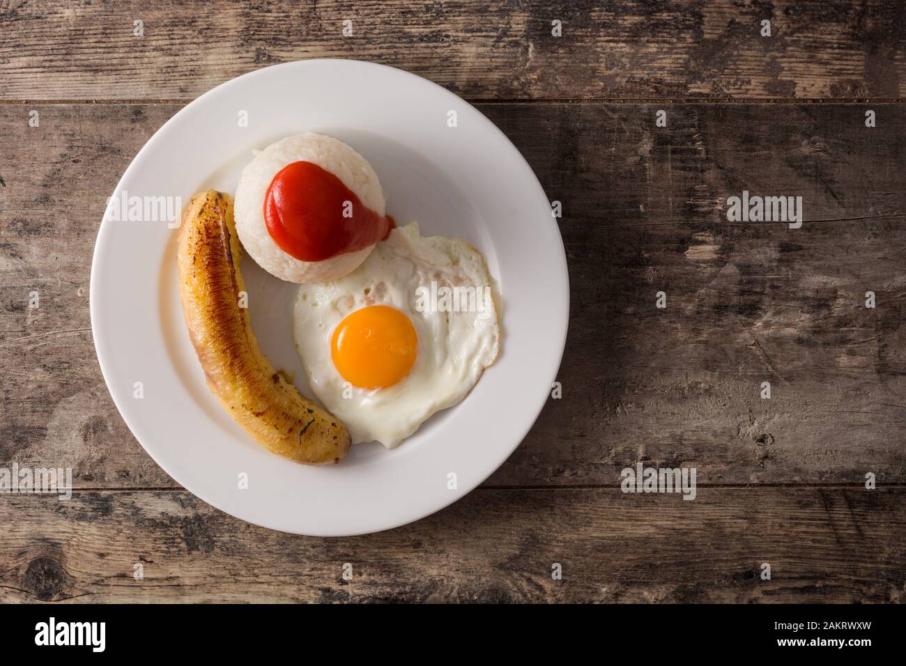 Arroz a la cubana Typical Cuban rice with fried banana and fried egg on a plate on wooden table. Top view. Copy space Stock Photo