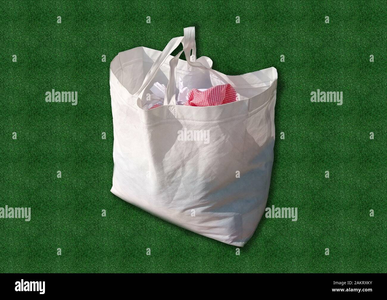White fabric cloth Recyclable ECO Bag on Green Grass background. Replacement plastic bag. Save Earth ecology. Non Woven Bag Good for the Environment. Stock Photo