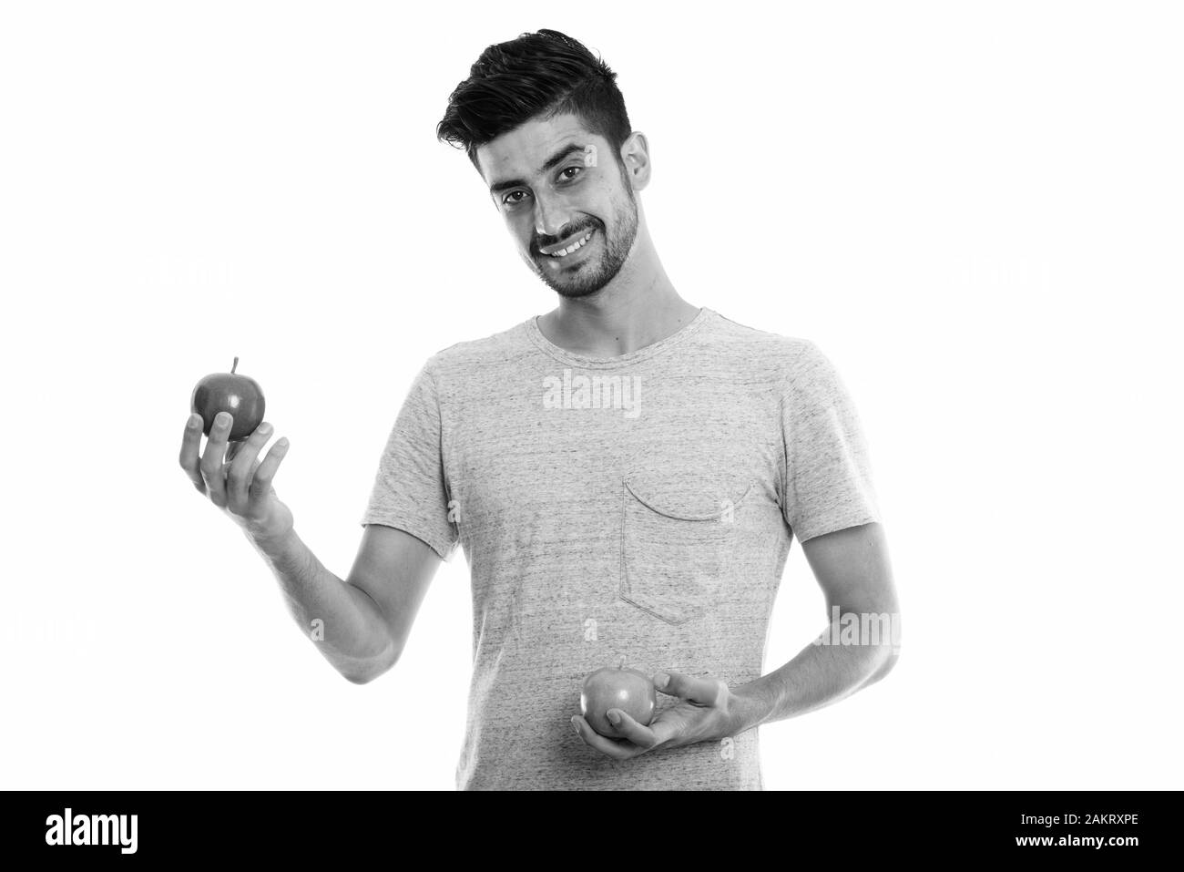 Studio shot of young happy Persian man smiling while raising red apple ...