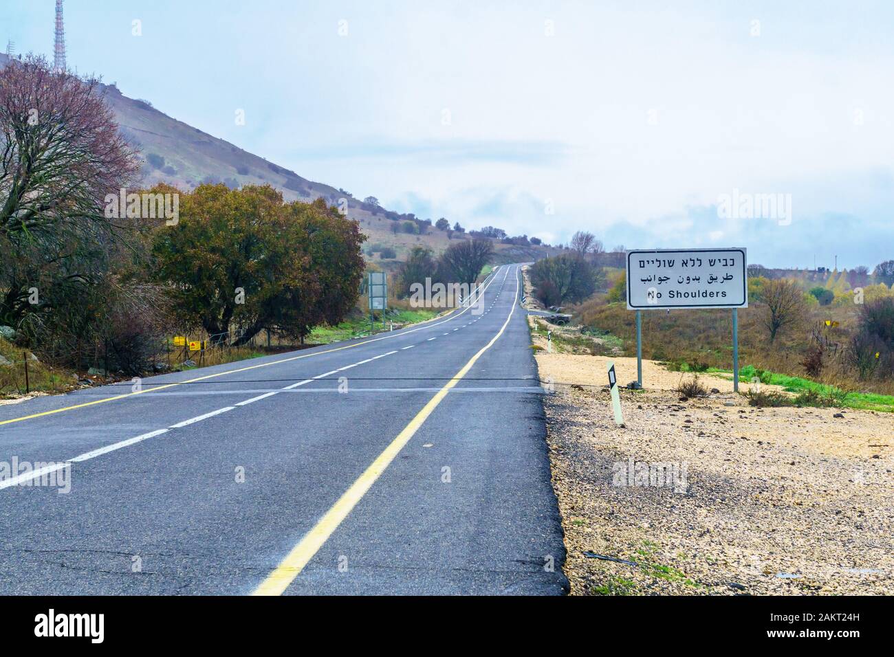 View of road and landscape in the Golan Heights, on a winter day, with trilingual warning sign: No Shoulders. Northern Israel Stock Photo