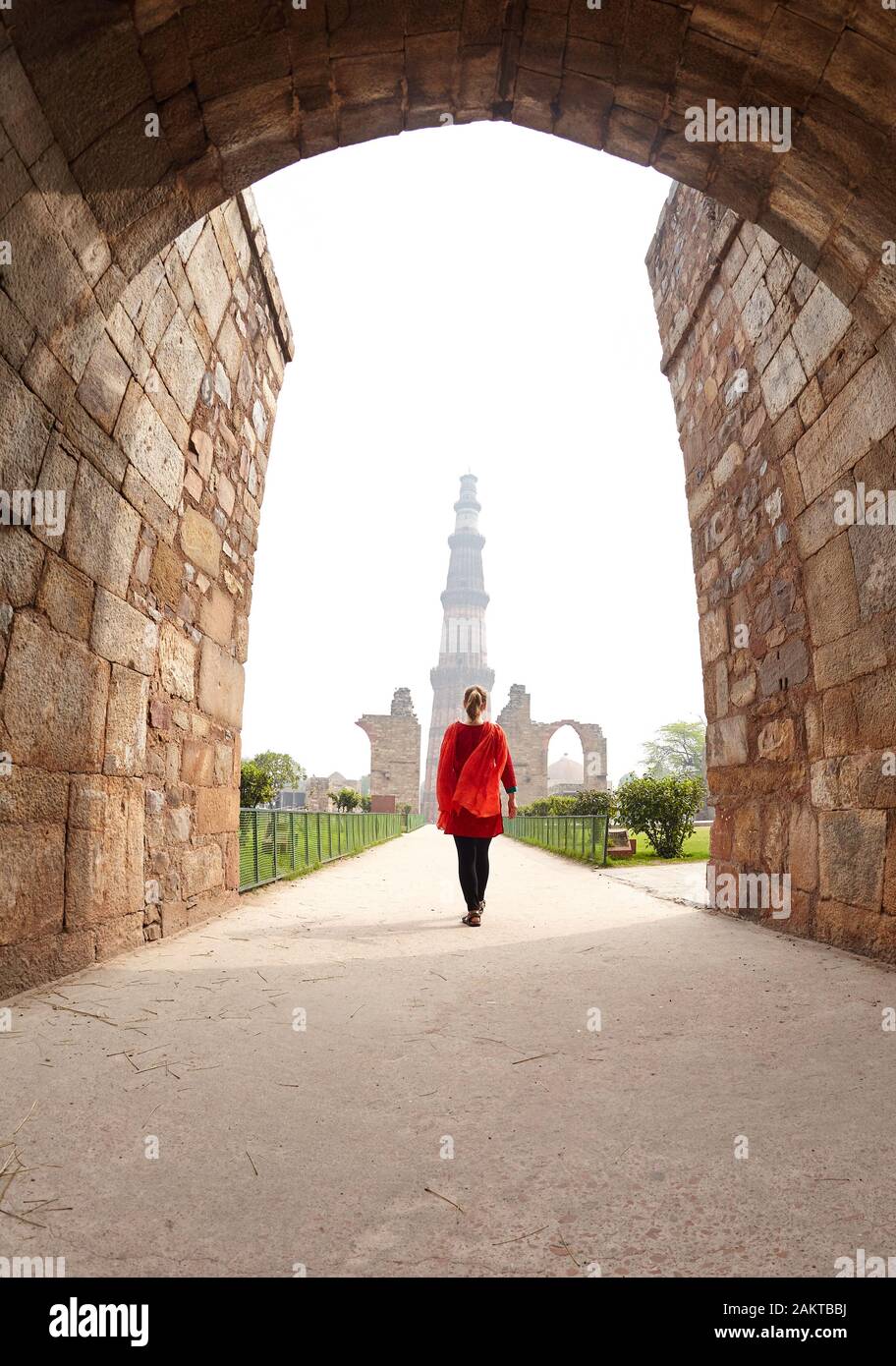Woman in red costume walking to Qutub Minar tower in Delhi, India Stock Photo