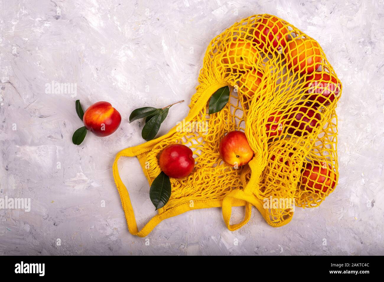 Nectarines in yellow string mesh reusable bag on the table Stock Photo