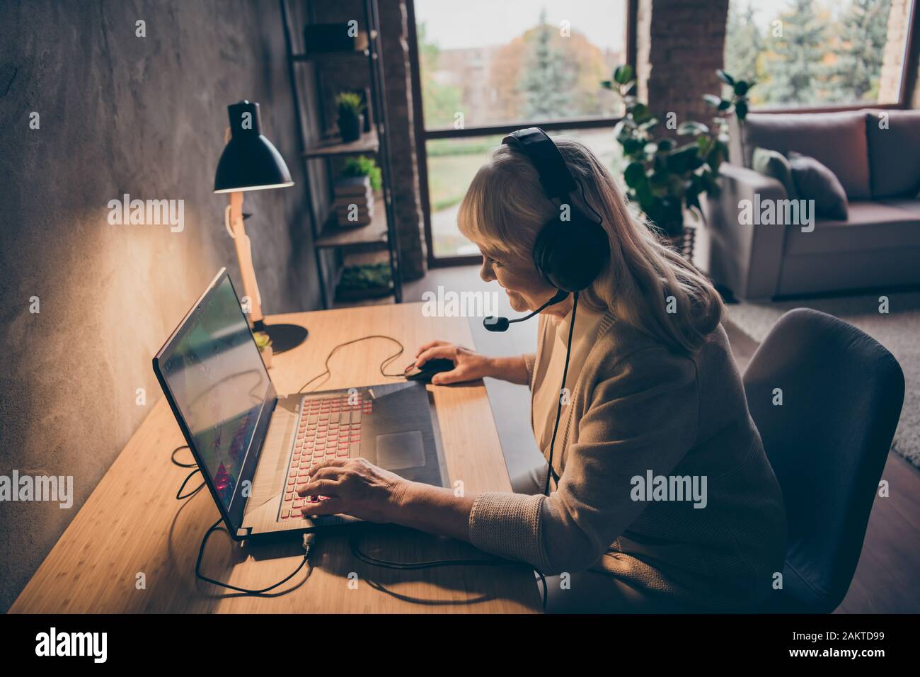 Profile side view portrait of nice attractive addicted cheerful cheery gray-haired blonde granny playing web net virtual VR game at industrial loft Stock Photo