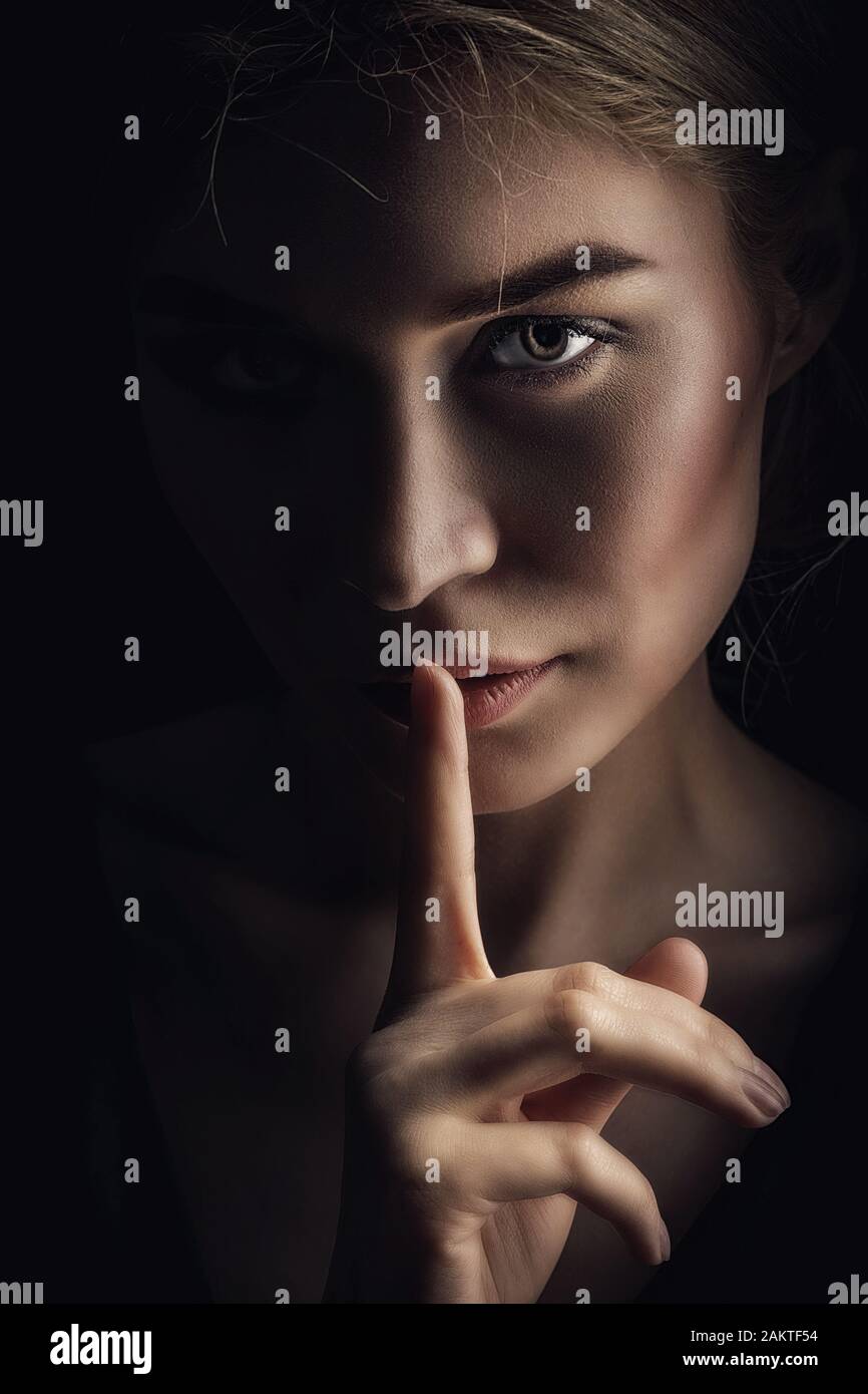 Girl shows a sign of silence. Face on a dark background. Dont Talk Concept Stock Photo