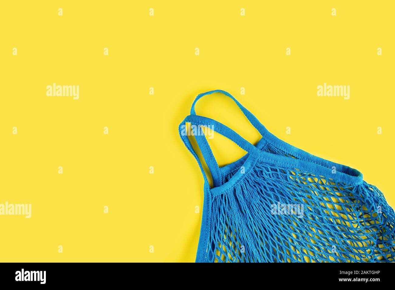 Blue reusable mesh on a yellow background. Ecological concept. Caring for the environment and rejection of plastic. Flat lay. Stock Photo