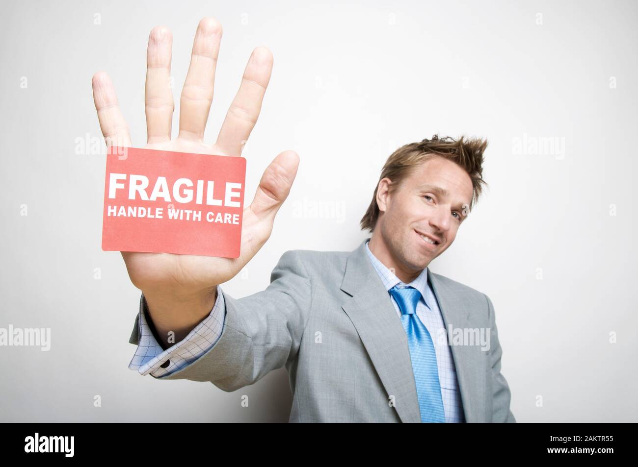 Smiling businessman holding out a Fragile Handle With Care sticker stuck to his palm Stock Photo