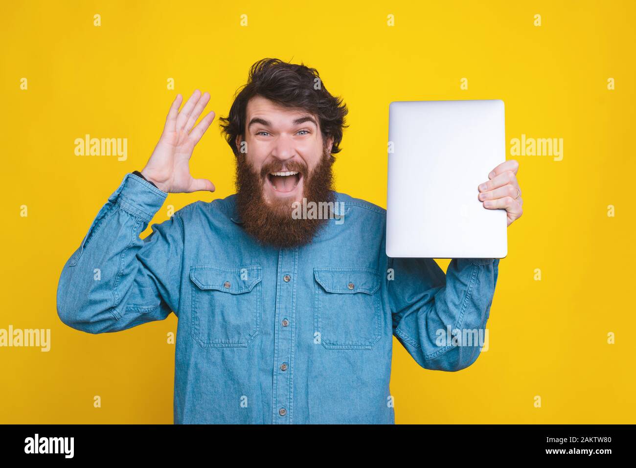 Photo of bearded hispter man holding new laptop over yellow background Stock Photo