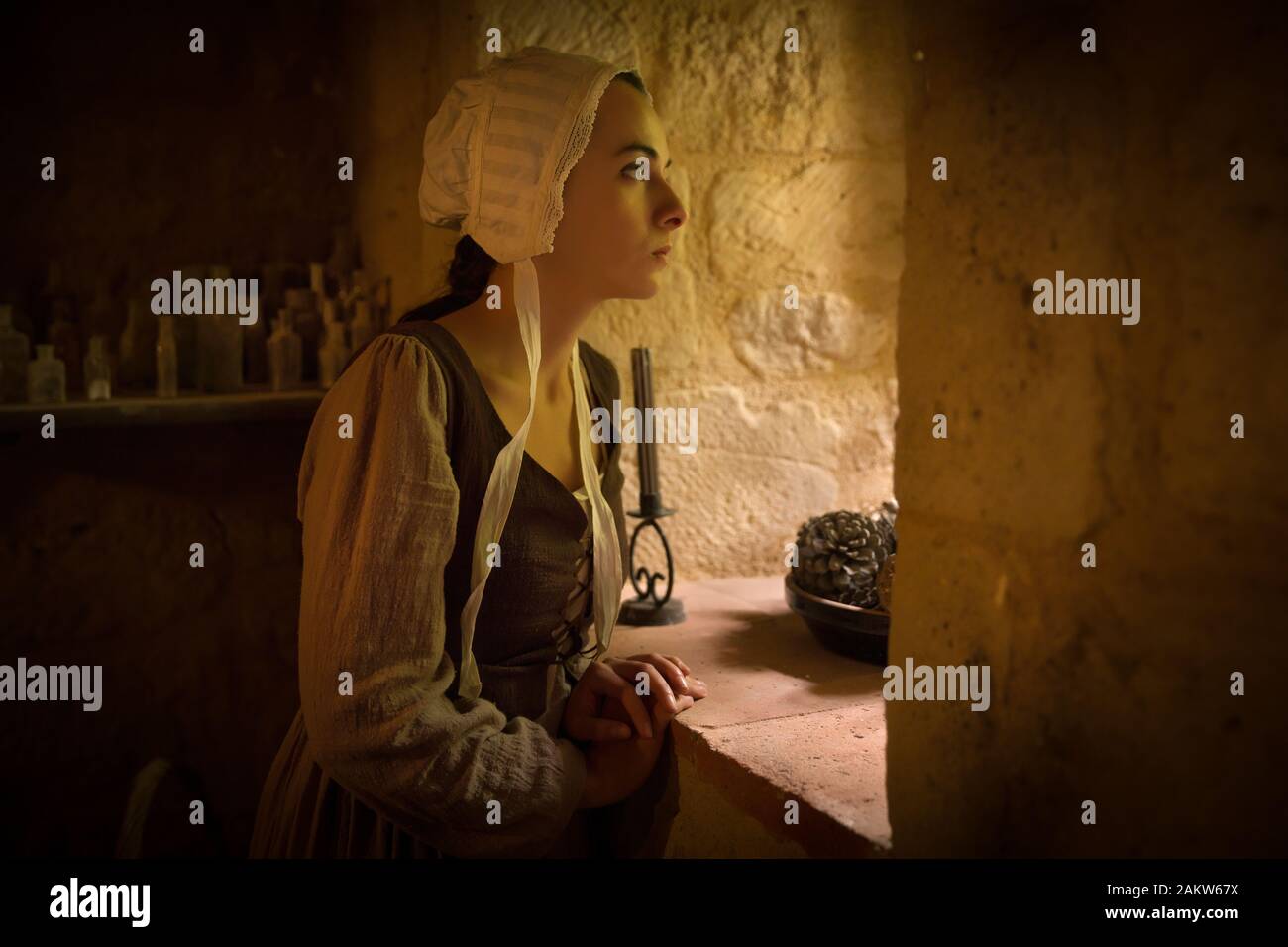 Vermeer style portrait of a young woman in Renaissance outfit looking out of the window of a medieval French castle - with property release Stock Photo