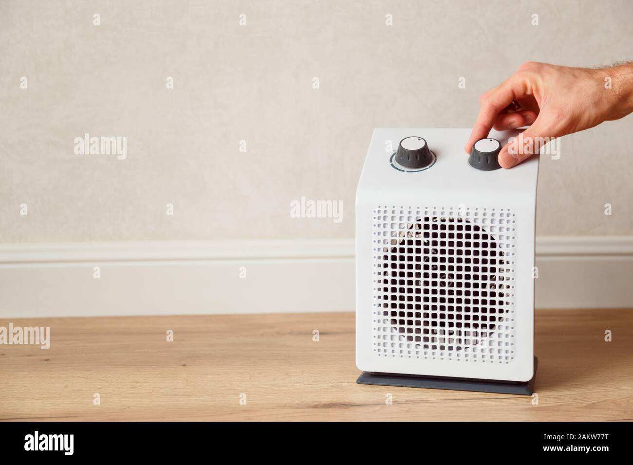 Man's hand adjusts the temperature of the electric fan heater at home in winter time. White domestic electric heater on floor indoor Stock Photo