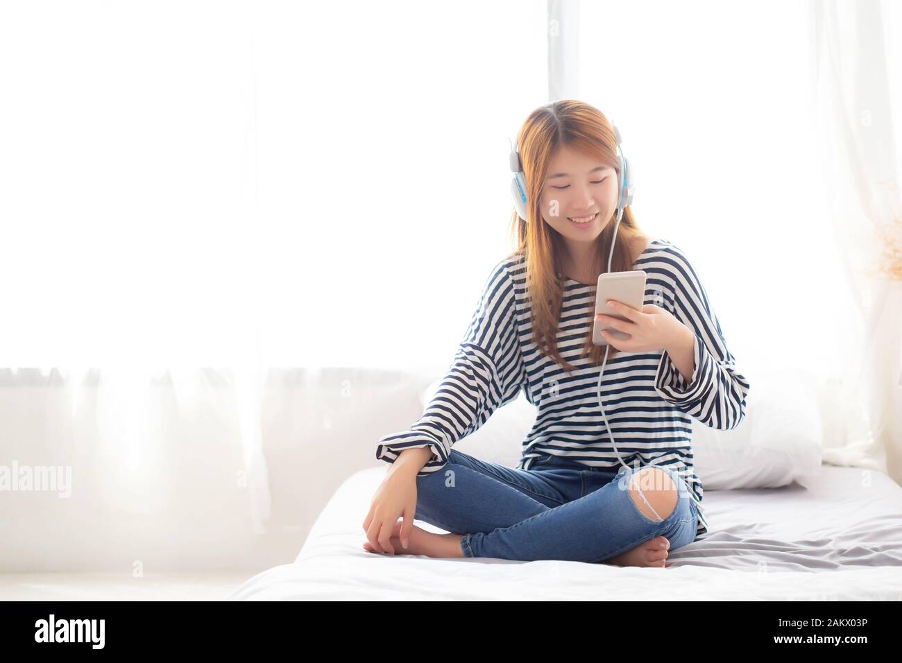 Beautiful asian young woman enjoy listen music with headphone and holding smart mobile phone while sitting in bedroom, relax girl with earphone, leisu Stock Photo