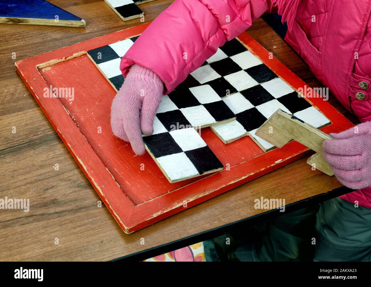 The child on the table collects wooden golovolomka. Stock Photo