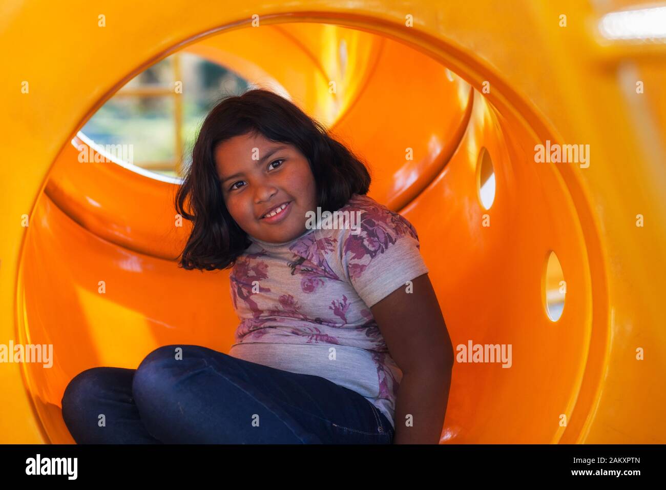 A cute latino girl with short hair playing in a kids playground, sitting  inside a circular tube slide Stock Photo - Alamy