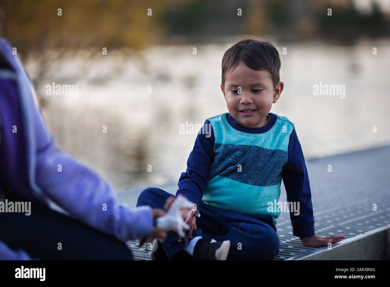 A little brother is playing with his older sister while sitting on the docks of a lake. Stock Photo