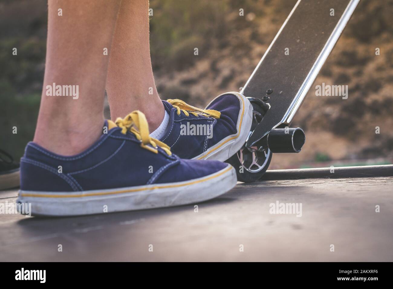 Close up view of teen's feet on a scooter ready to start a ride over the half pipe. Skater starting jumps and tricks at the skate park. Let's go enjoy Stock Photo