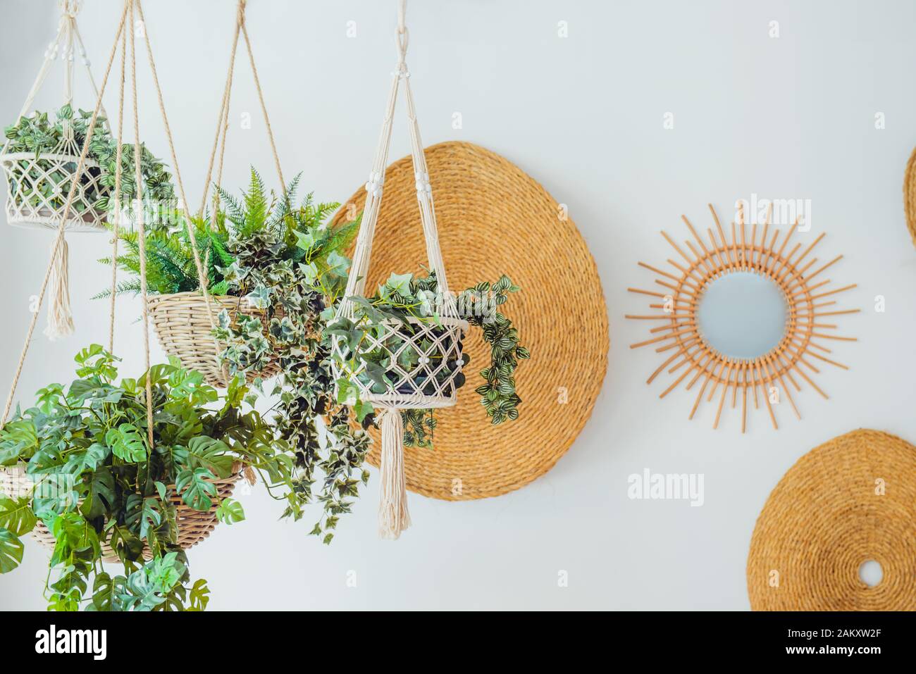 Modern minimal Scandinavian home interior design. Straw round decor with hanging flower pots with green plants on the white wall background. Eco natur Stock Photo