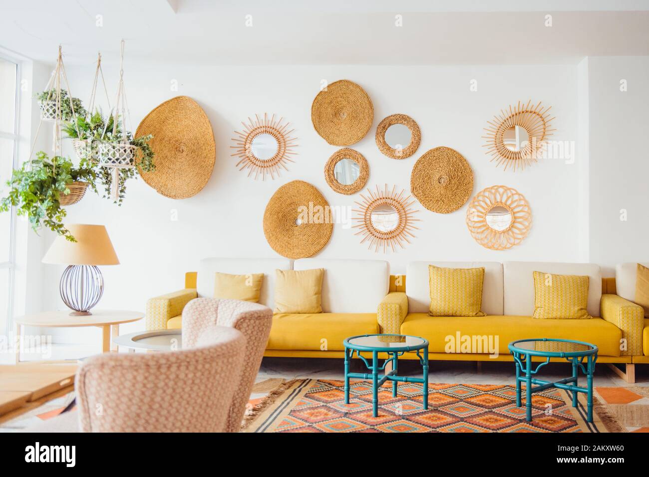 Modern minimal home interior design. Yellow sofa with pillows, green tables, fresh green plants in hanging pots, decorative straw decor, Scandinavian Stock Photo