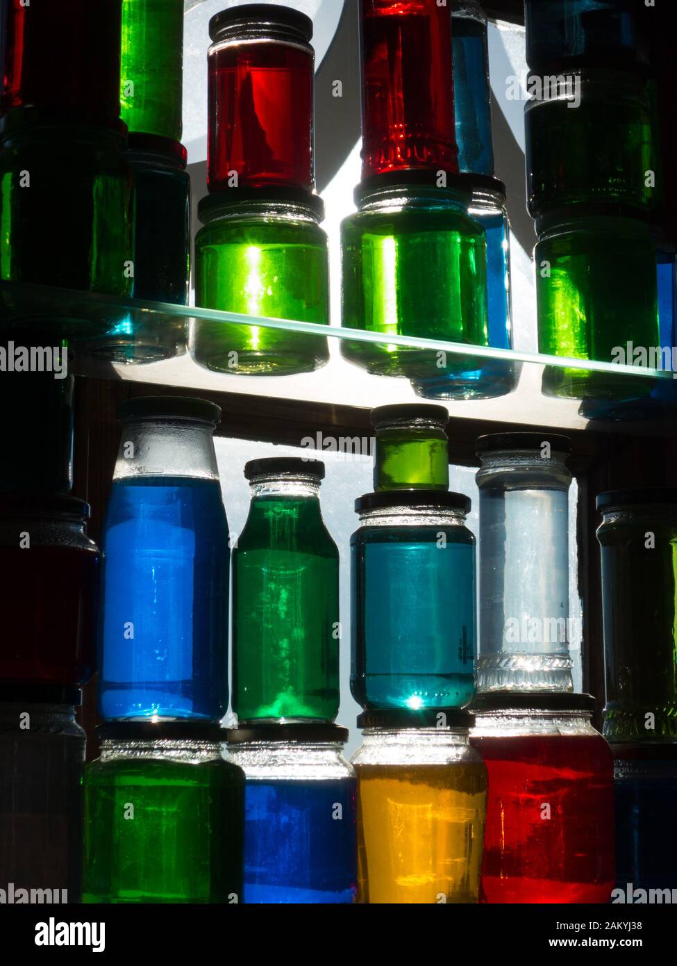 Traditional icelandic window decoration with shining jars filled with colored water. Shot against sunlight with whole array of colors visible. Stock Photo
