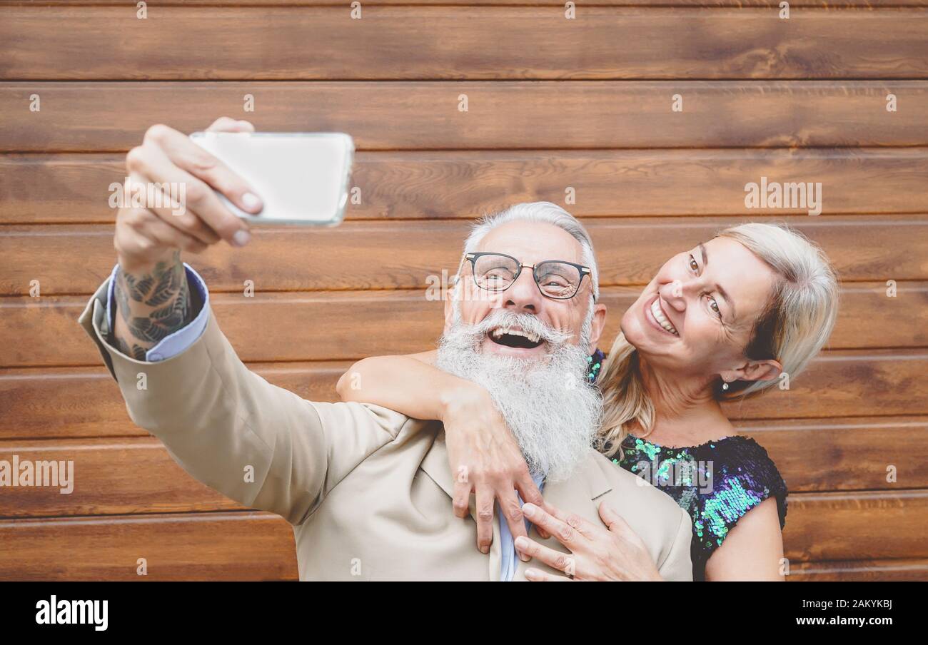 Seniors couple laughing and taking selfie with mobile smartphone camera - Social mature people having fun with new trendy technology Stock Photo