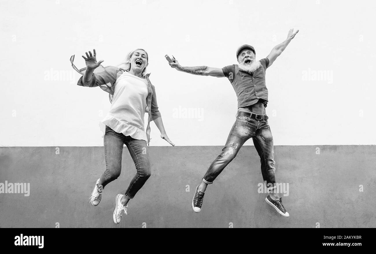 Happy crazy senior couple jumping together outdoor - Mature trendy people having fun celebrating and dancing outside Stock Photo