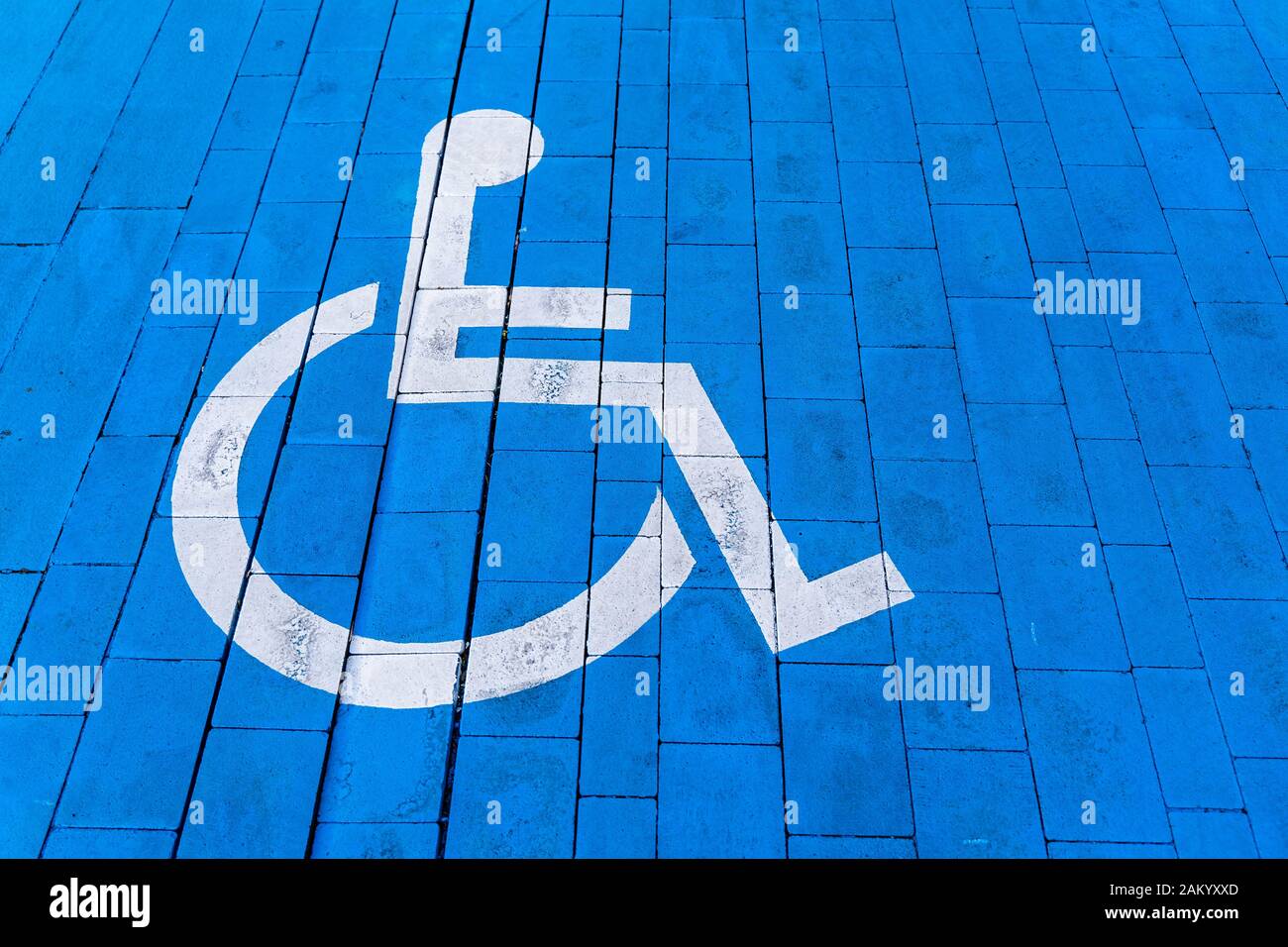 Wheelchair with information sign on brick floor, parking place for disable. White painted symbol on blue ground. Stock Photo