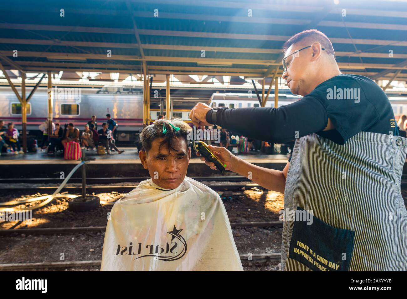 Bangkok/Thailand-December 2019: A street barber giving free haircut to his male client on a train platform  at Hua Lamphong train station. Stock Photo