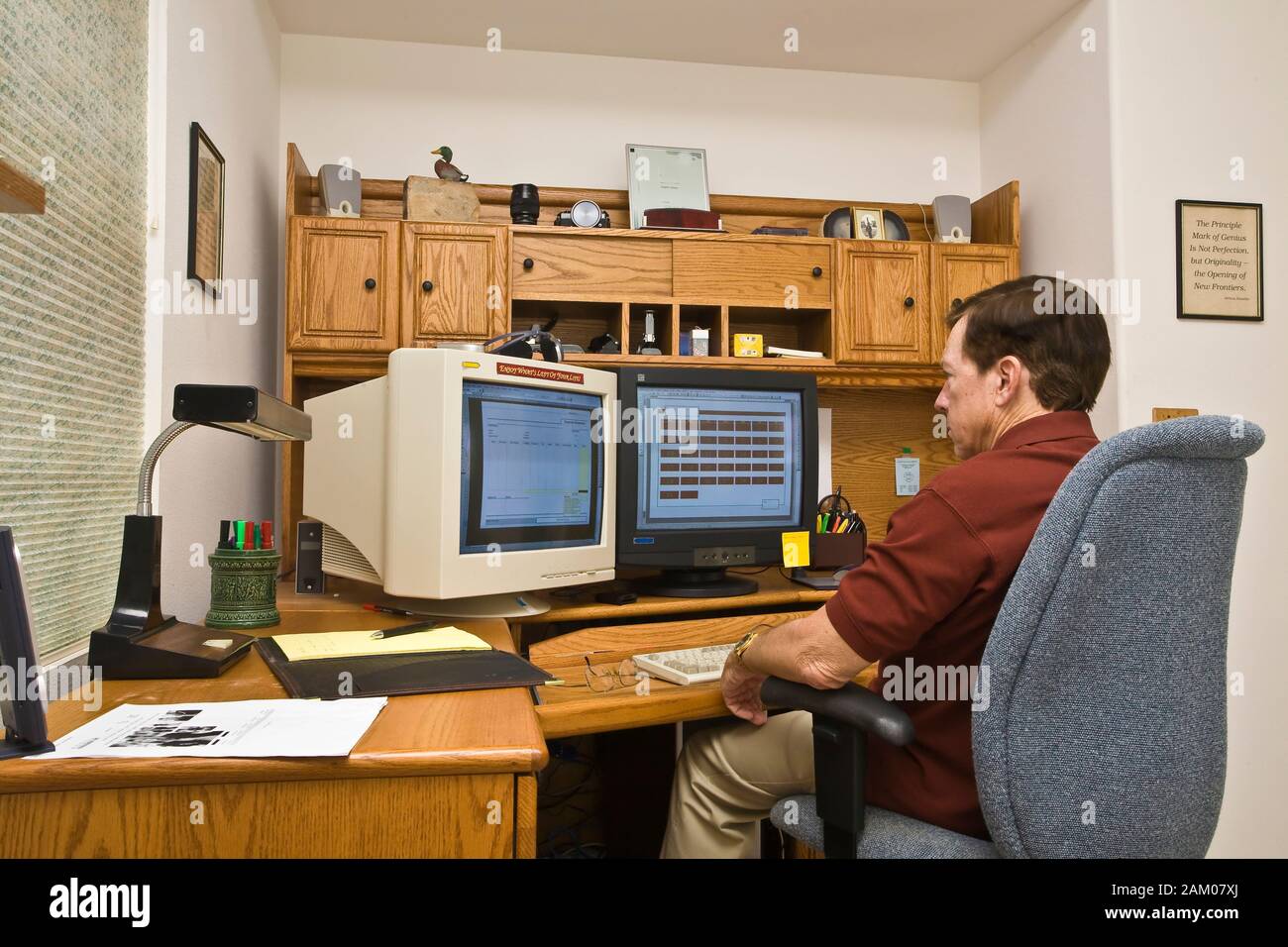 Older Man Sitting In Office Chair At Computer Desk With Dual