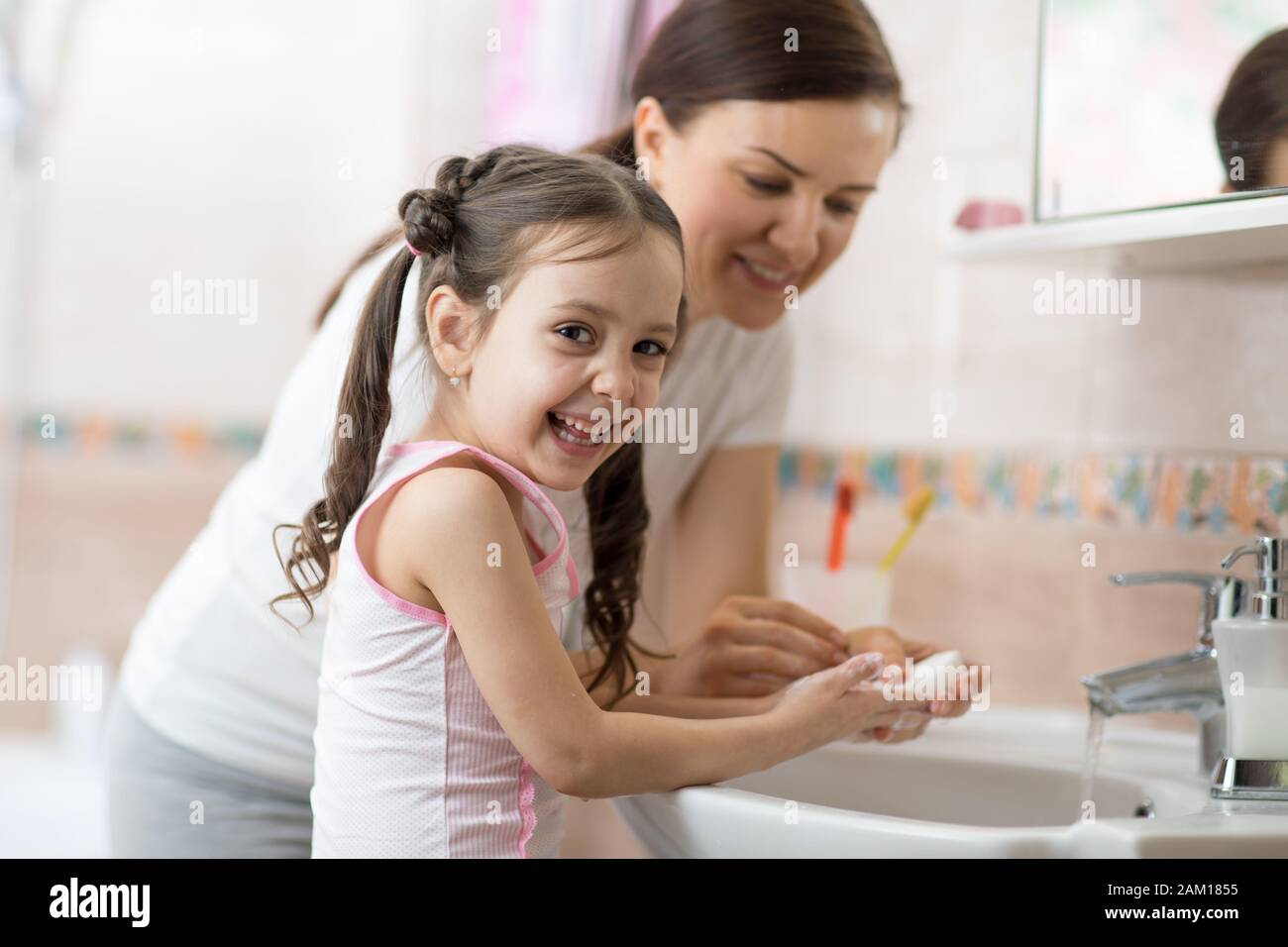 Woman and her daughter child washing hands with soap in bathroom Stock Photo