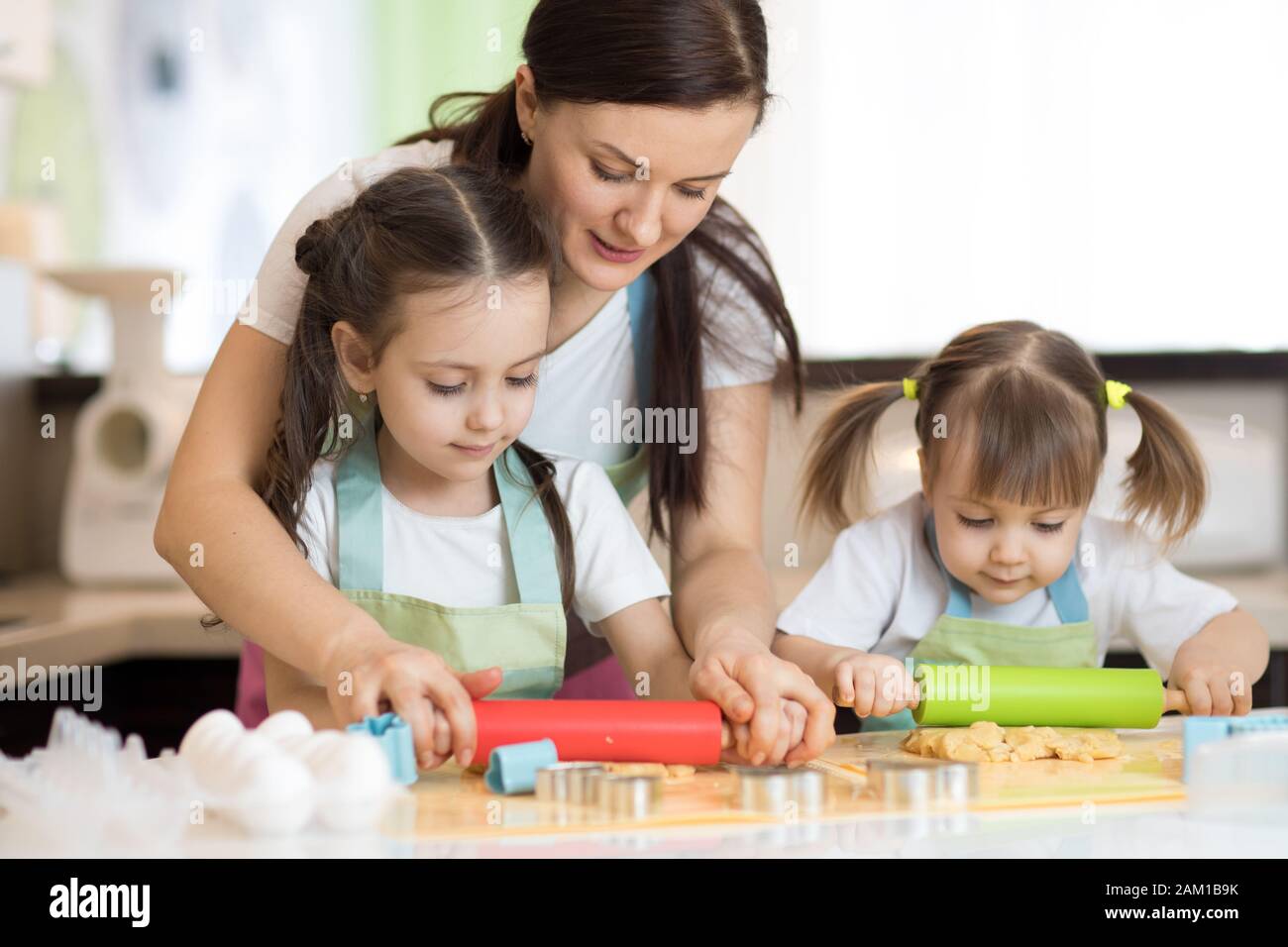 Adorable mother and her kids daughters cooking together in the kitchen Stock Photo