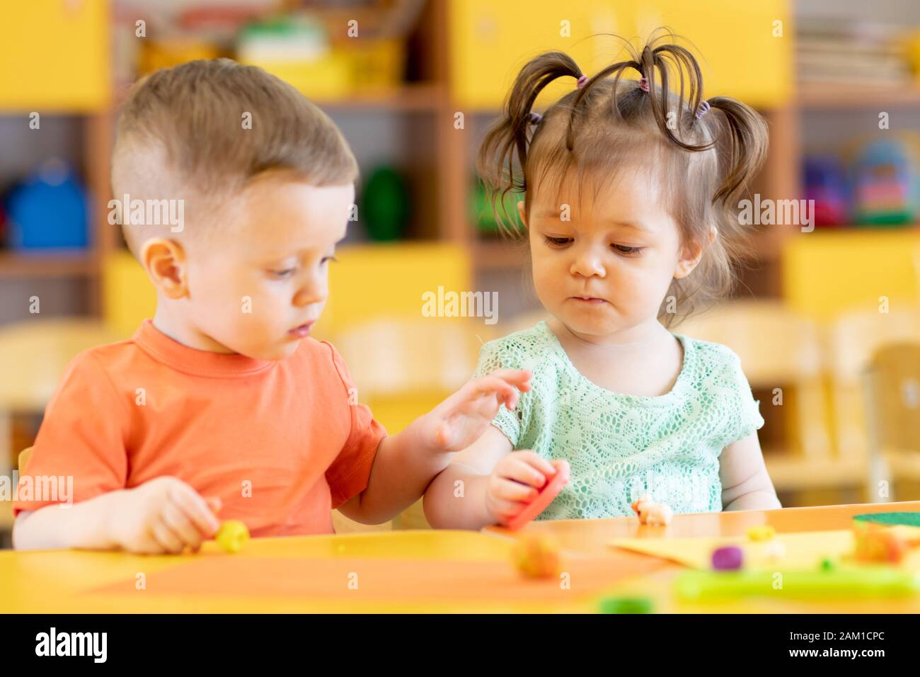 Toddlers boy and girl playing at table with educational toys. Children infants in creche or daycare. Stock Photo