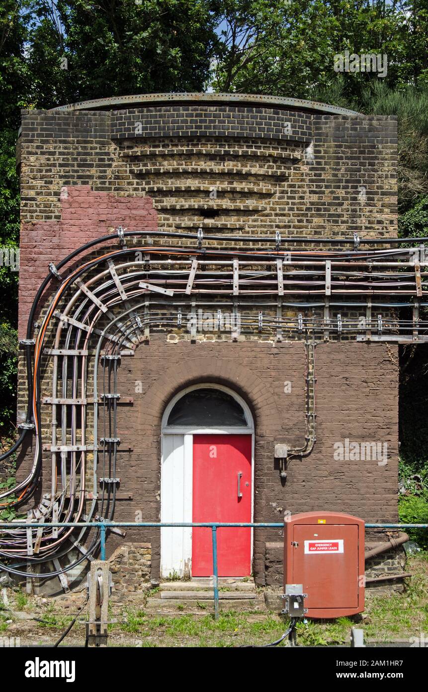 A small brick Art Deco building covered in electrical cables in the sidings at Ealing Broadway station in West London. Stock Photo