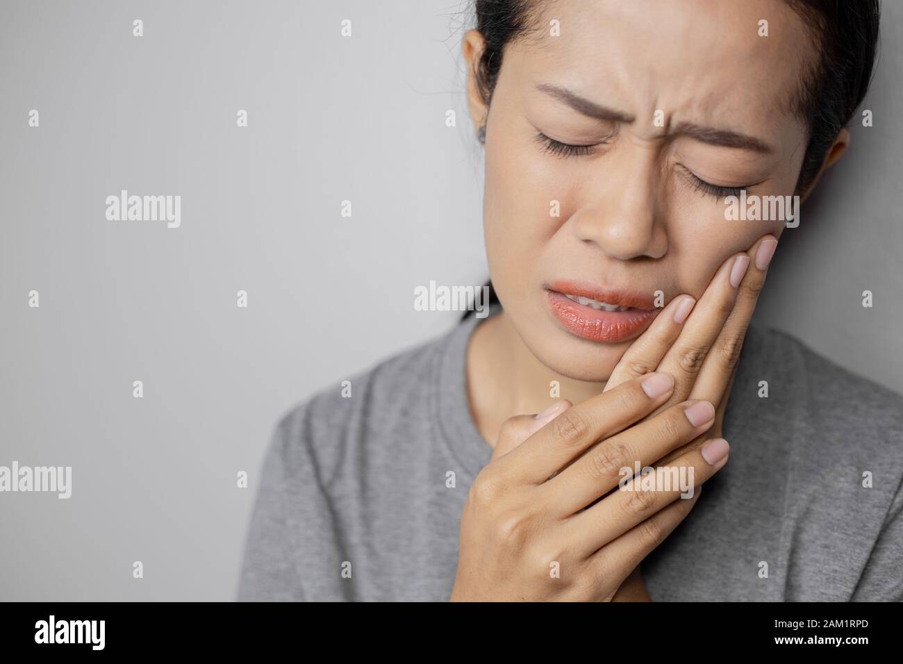 Woman put her hand on her cheek due to toothache. Asian  woman is suffering of toothache. Young woman with of toothache on a gray background. Stock Photo