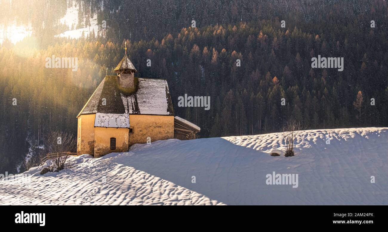 mountain landscape, panoramic snow slope with church in winter day with sun flare and lens flare Stock Photo