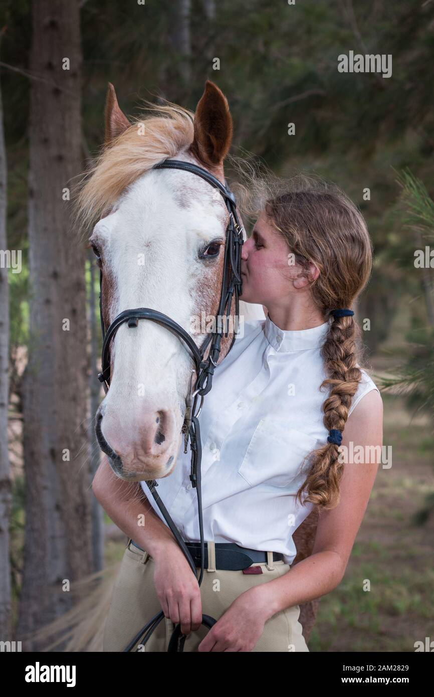 Girl standing next to her Sabino paint horse both facing the camera close up of the girl kissing the horse. Stock Photo